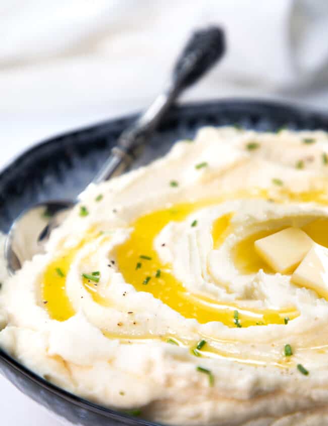 a close up image of Sour Cream Mashed Potatoes with melted butter and chopped chives