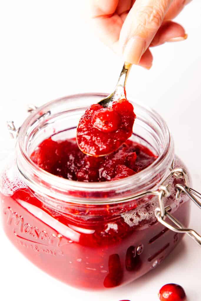 a hand holding a spoonful of Homemade Fresh Cranberry Sauce