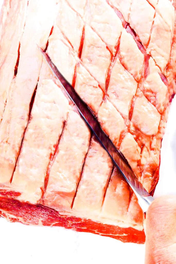 a knife making cuts into the fat of a ribeye roast
