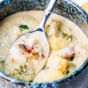 a bowl and spoon full of cream od crab soup with potatoes, cellery and crab meat