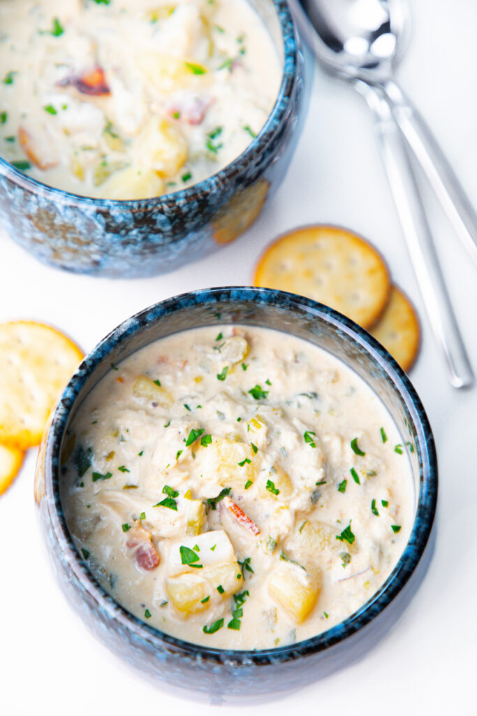 two bowls of cream of crab soup with crackers and spoons in the background