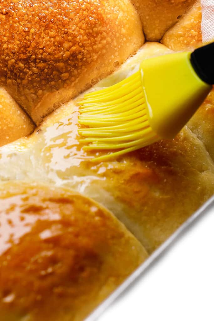 Applying butter on top of freshly baked homemade yeast dinner rolls.