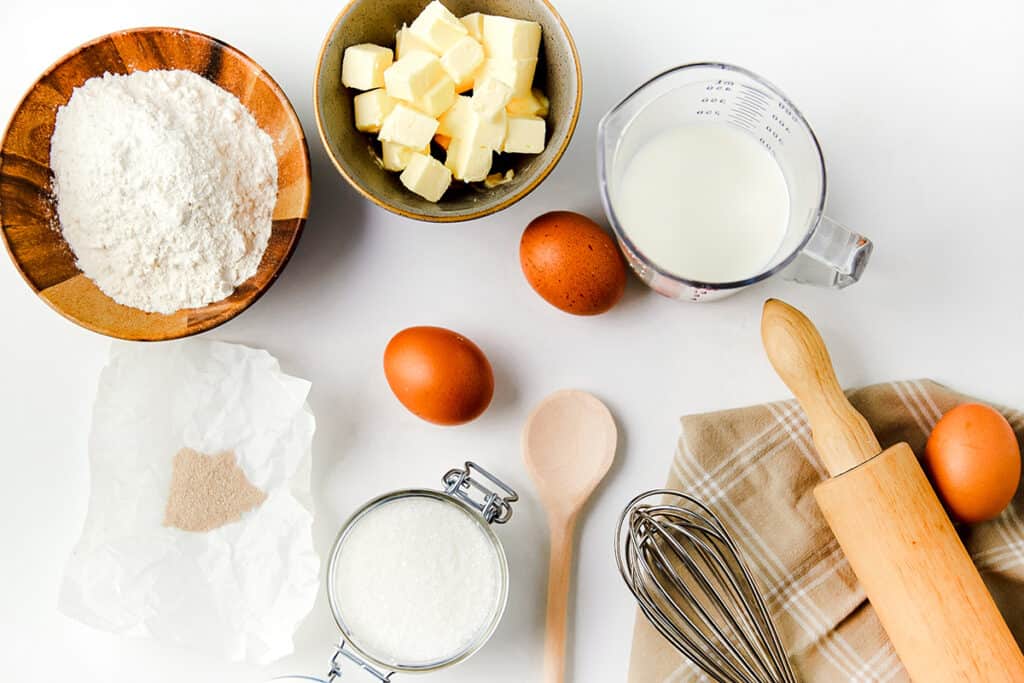 flour, butter, bilk, eggs, yeast, sugar, and salt on a table