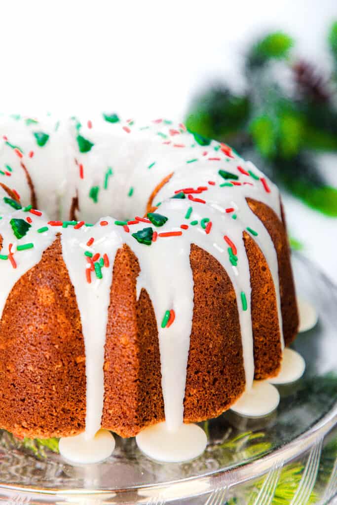 a close up image of an eggnog bundt cake topped with glaze and holiday sprinkles