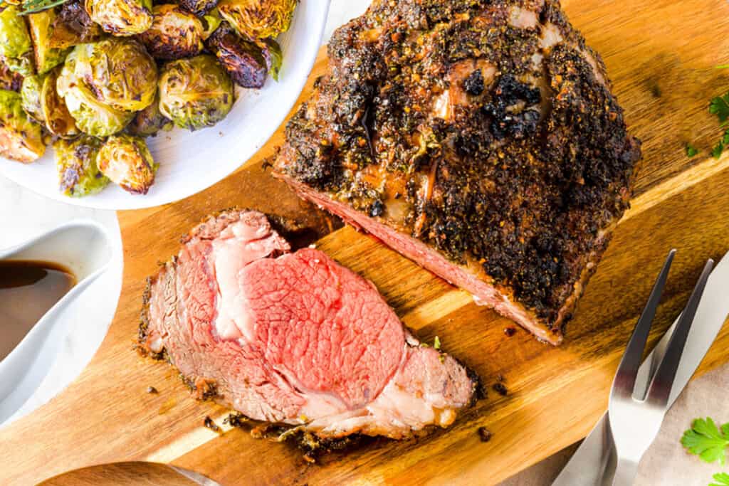 an over head shot of the carved ribeye roast with brussels sprouts and gravy next to it