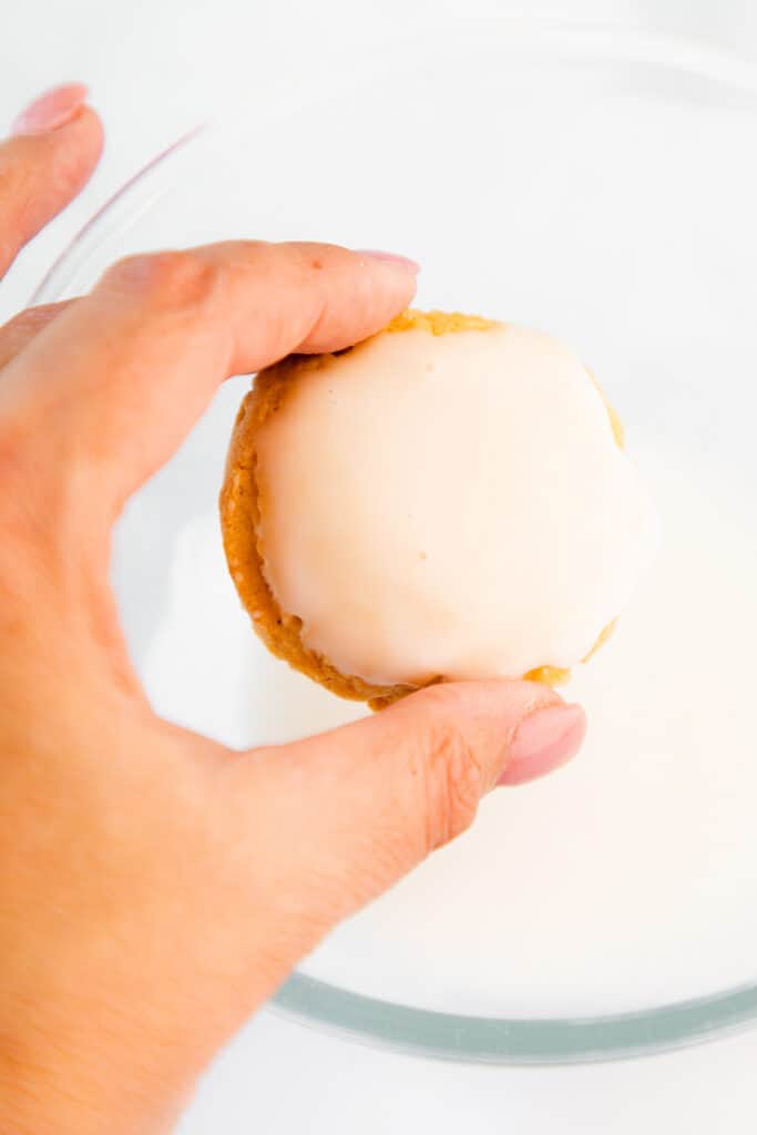 a woman holding a iced cookie over a bowl of icing
