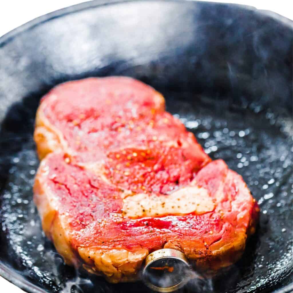 a raw steak cooking in a hot pan