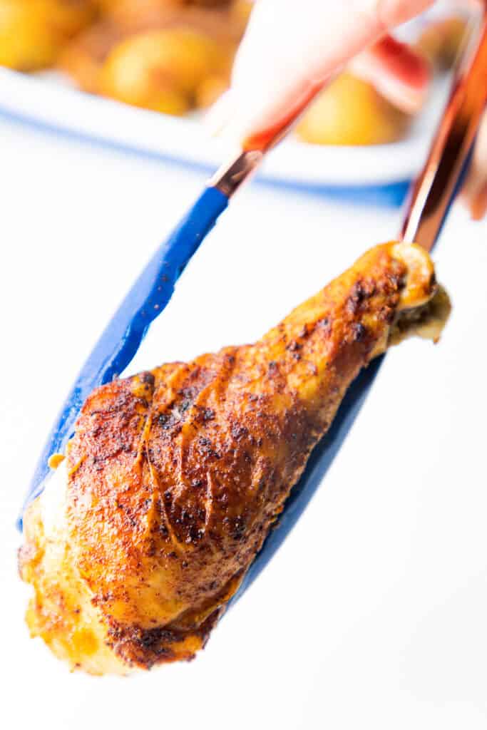 a pair of tongs holding a baked chicken leg