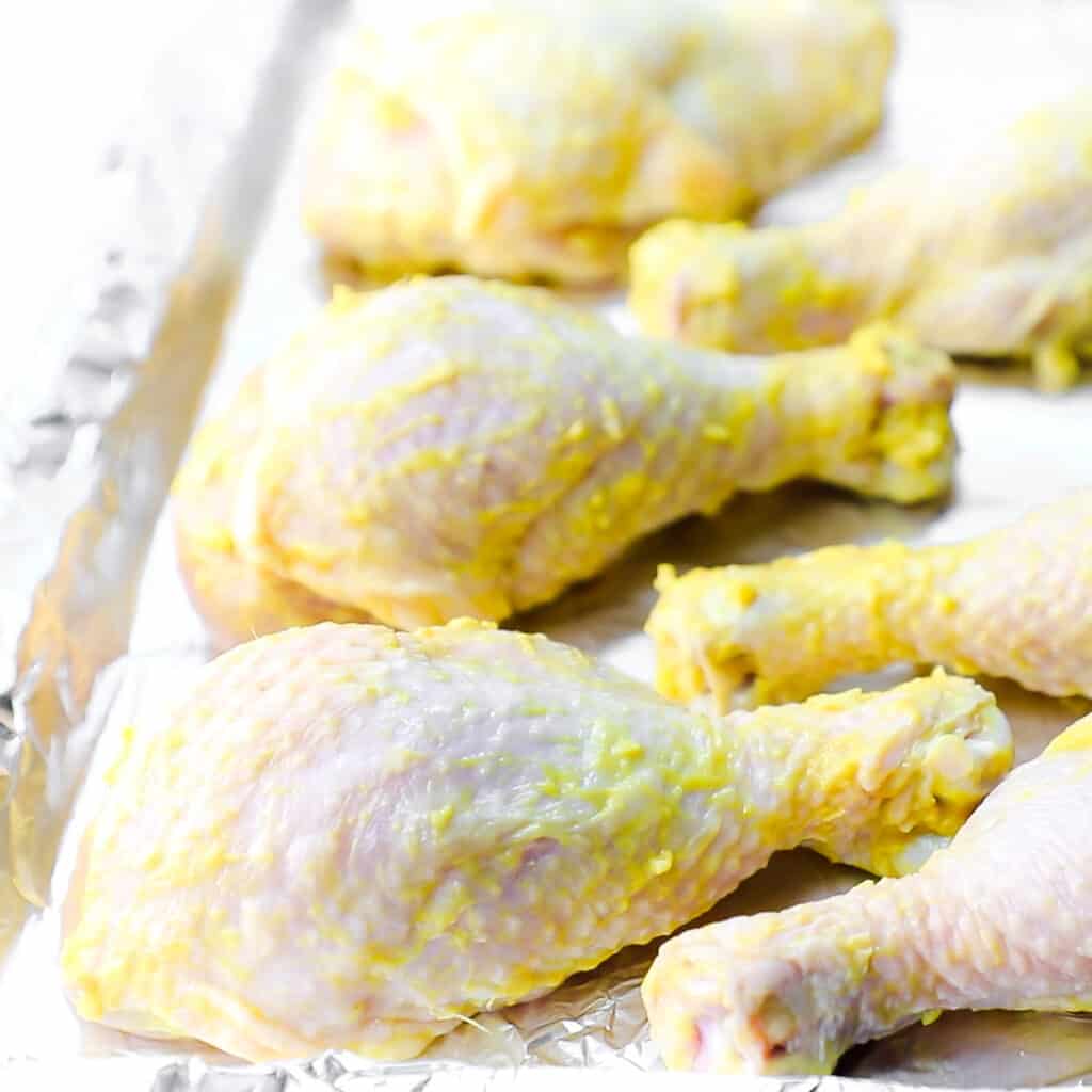 the chicken legs coated in the mustard mixture on a baking sheet lined with foil