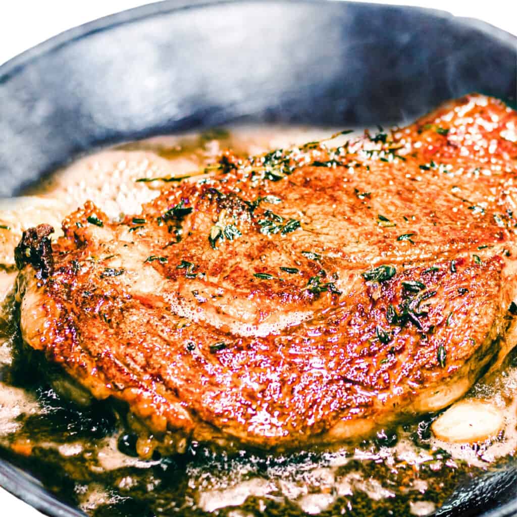 the cooked steak in the pan with garlic and herbs