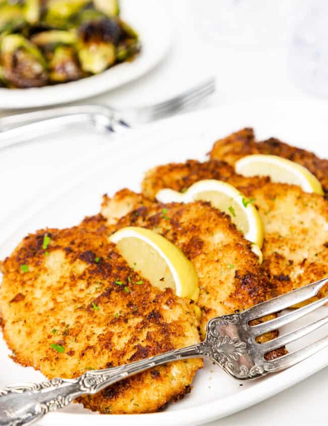 a serving dish with 4 slices of breaded panko chicken garnished with lemon wedges