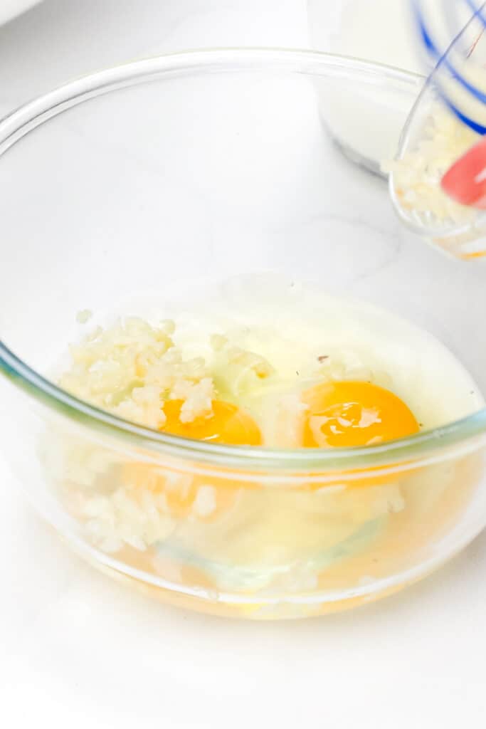 garlic and milk added to the eggs in a bowl