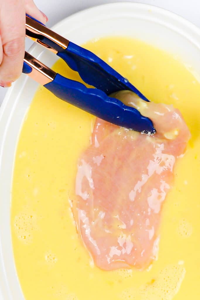 a slice of chicken being dipped into the egg mixture