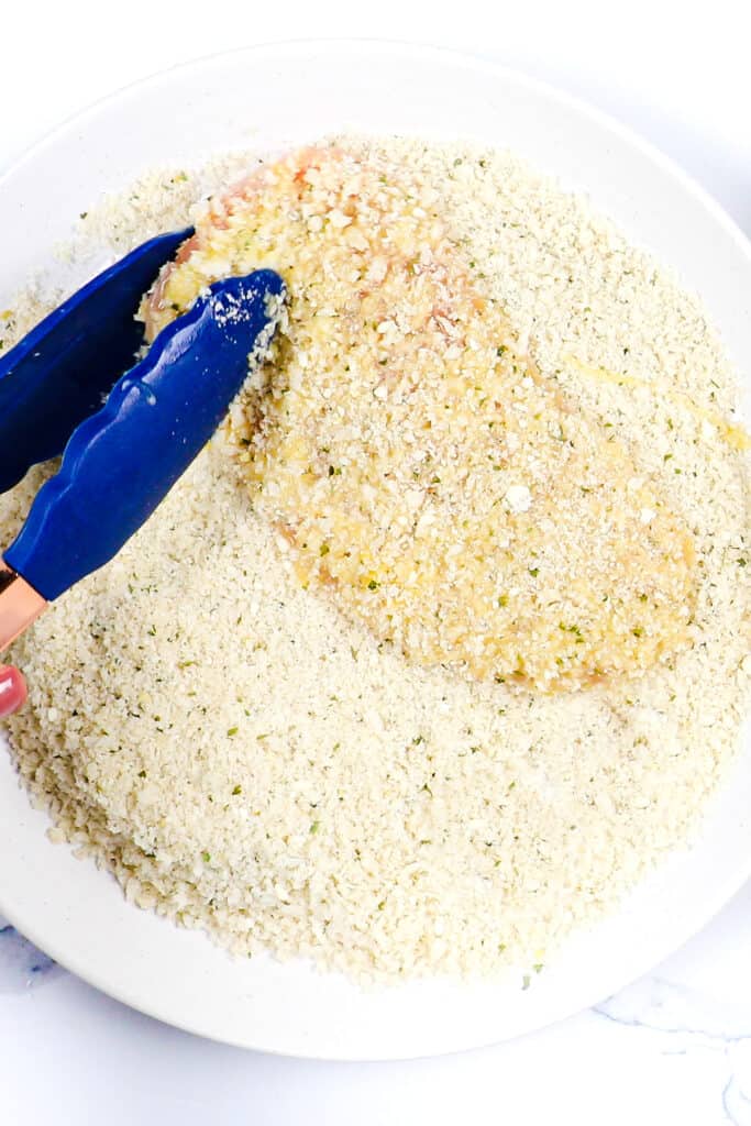 the egg coated chicken being coated with panko breadcrumbs