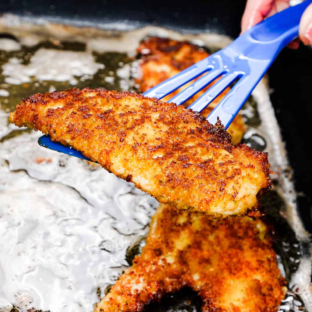 a slice of cooked panko chicken being lifted from the pan with a spatula 