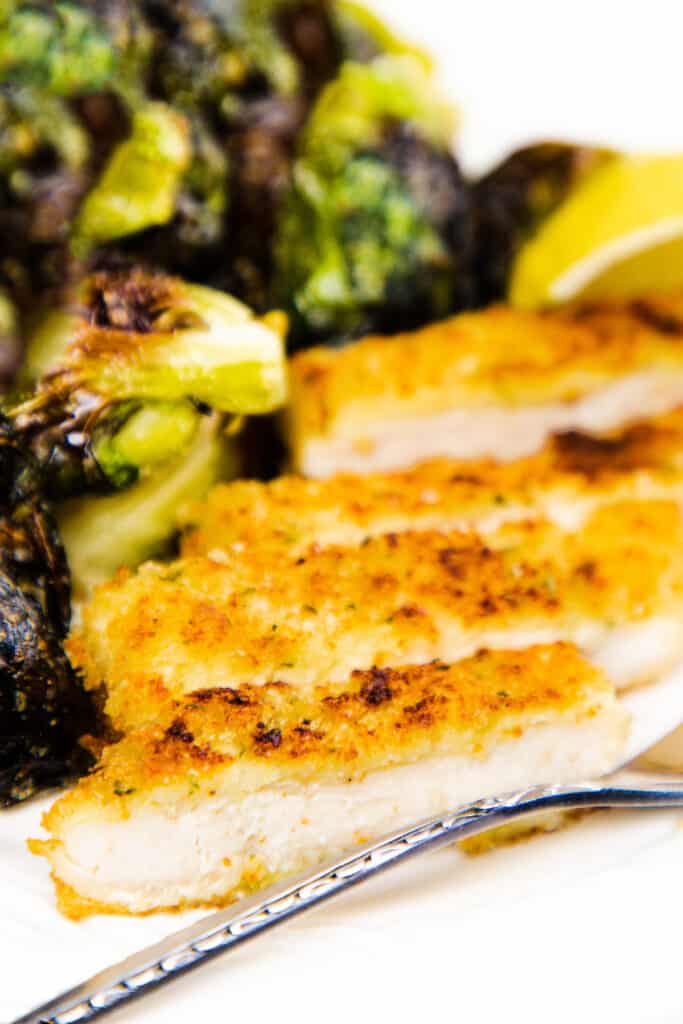 a sliced serving of Panko chicken on a plate with roasted brussels sprouts