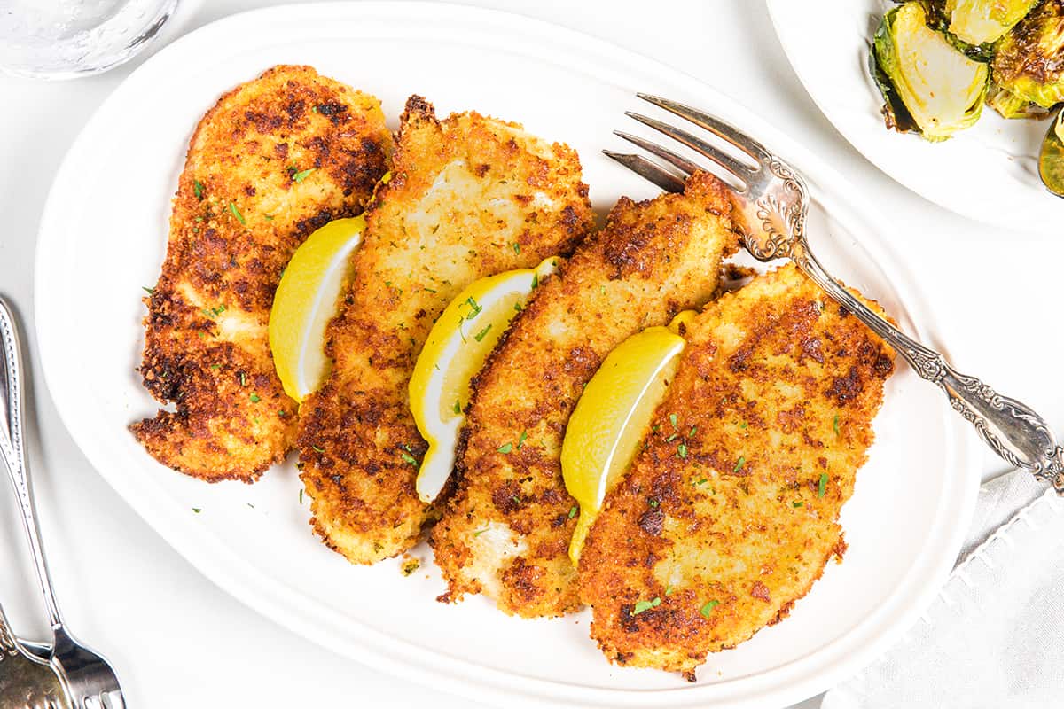 an overhead image of Panko Chicken on a plate with a fork and lemon wedges