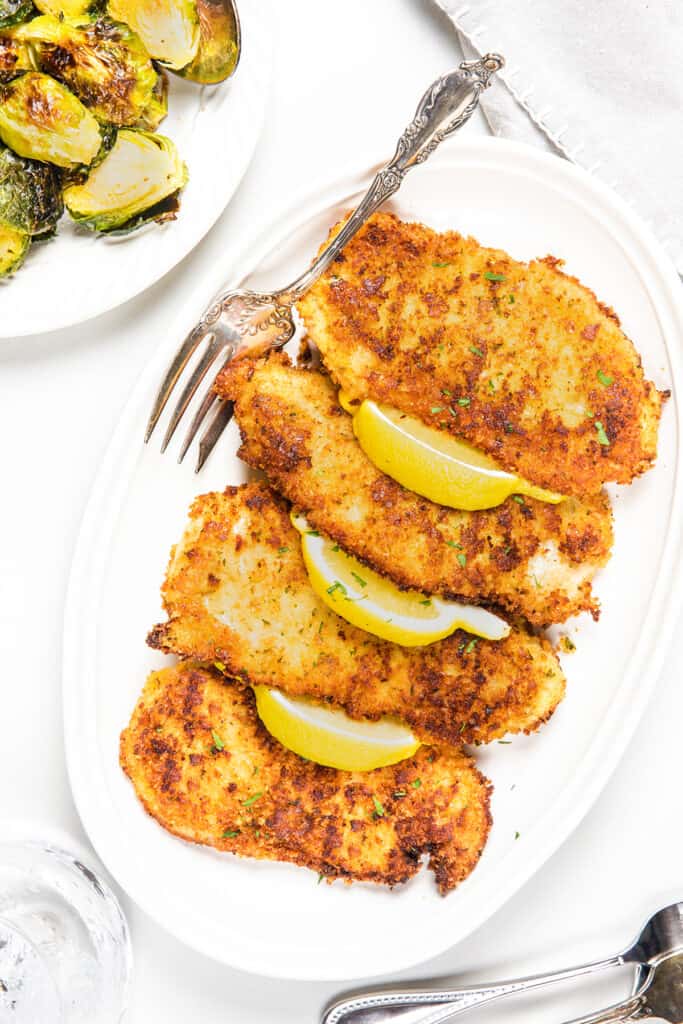 an overhead image of 4 panko chicken cutlets on a serving platter with lemons and a serving fork