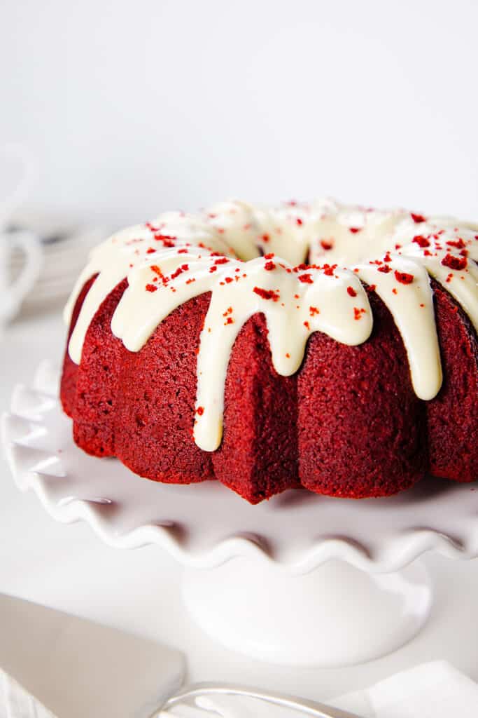 a cake stand with a Red Velvet Bundt Cake topped with white icing