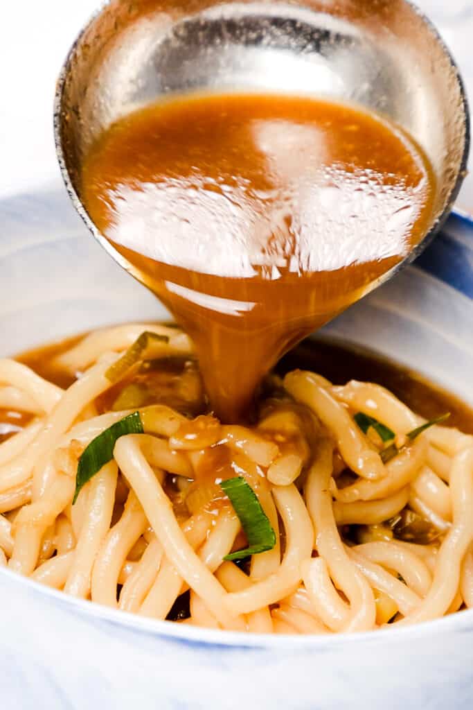 thee broth being spooned into a bowl with udon noodles