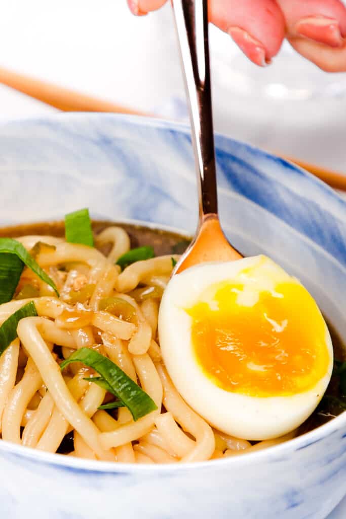 a soft boiled egg being added to a bowl of Udon Soup