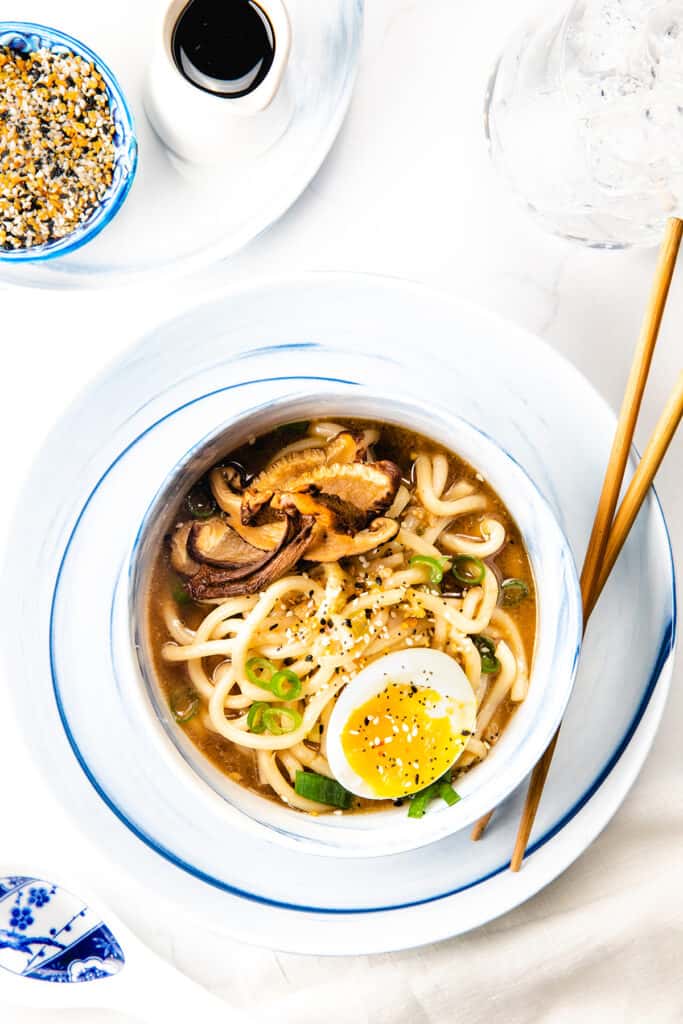 an overhead image of a bowl of Udon Soup topped with mushrooms, scallions, and a soft boiled egg