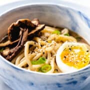 a close up image of of a bowl of Udon Soup topped with mushrooms, scallions, and a soft boiled egg