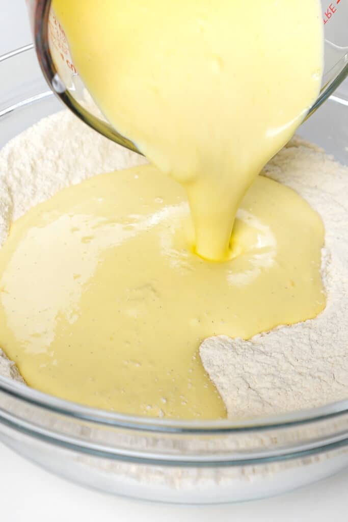 the wet ingredients being poured into the bowl with the flour mixture