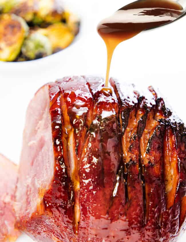 a honey glaze being spooned onto a honey glazed ham