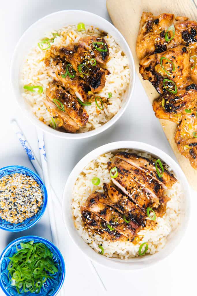 two bowls of rice topped with sliced miso chicken garnished with green onions and sesame seeds