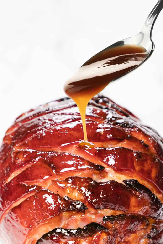the glaze being drizzled onto the baked Honey Glazed Ham