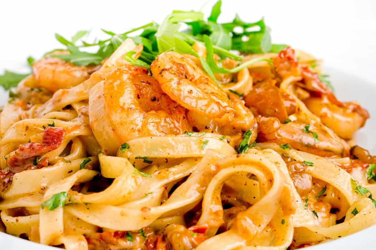 a landscape image of a white plate full of shrimp pasta