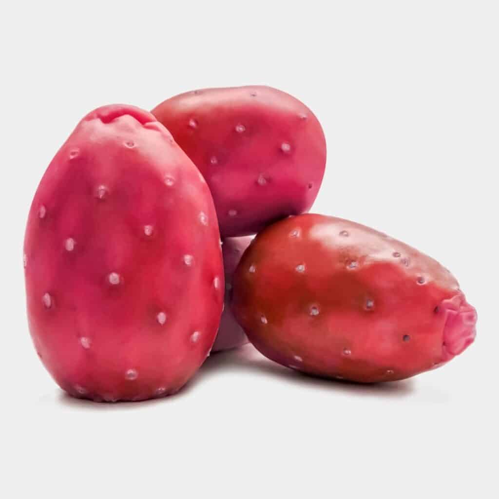 three Xoconostle prickly pears sitting on a white table