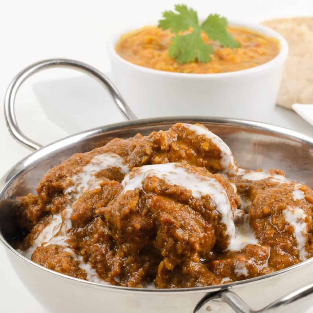 a Xacuti curry in a silver bowl with a bowl of dal behind it