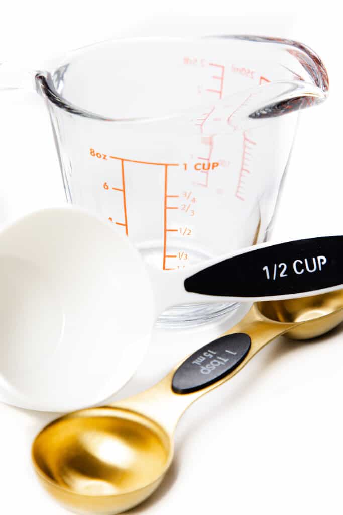 a photo showing a glass measuring cup, a plastic 1/2 cup measuring cup and a gold tablespoon measuring spoon