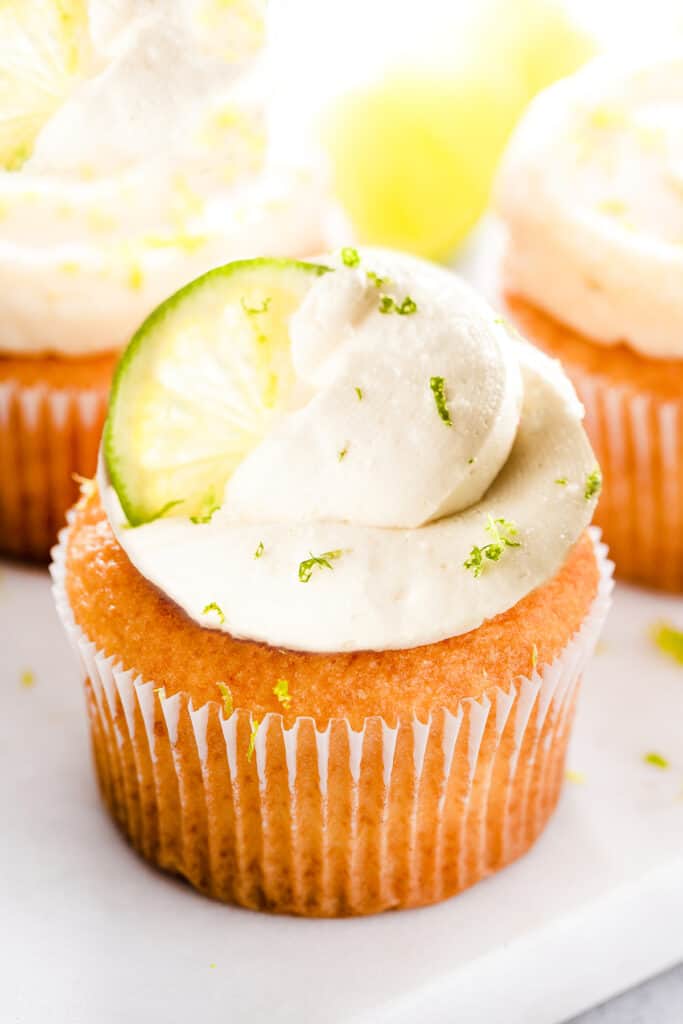 three key lime cupcakes on a plate decorated with a slice of lime and lime zest.