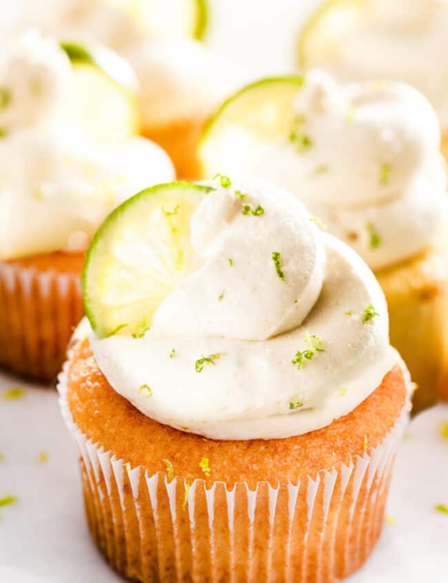 a platter of key lime cupcakes with a swirl of cream cheese frosting and a slice of lime to decorate