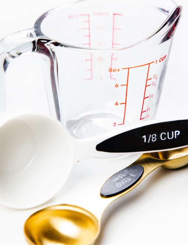 a photo showing a glass measuring cup, a plastic 1/8 cup measuring cup and a gold tablespoon measuring spoon