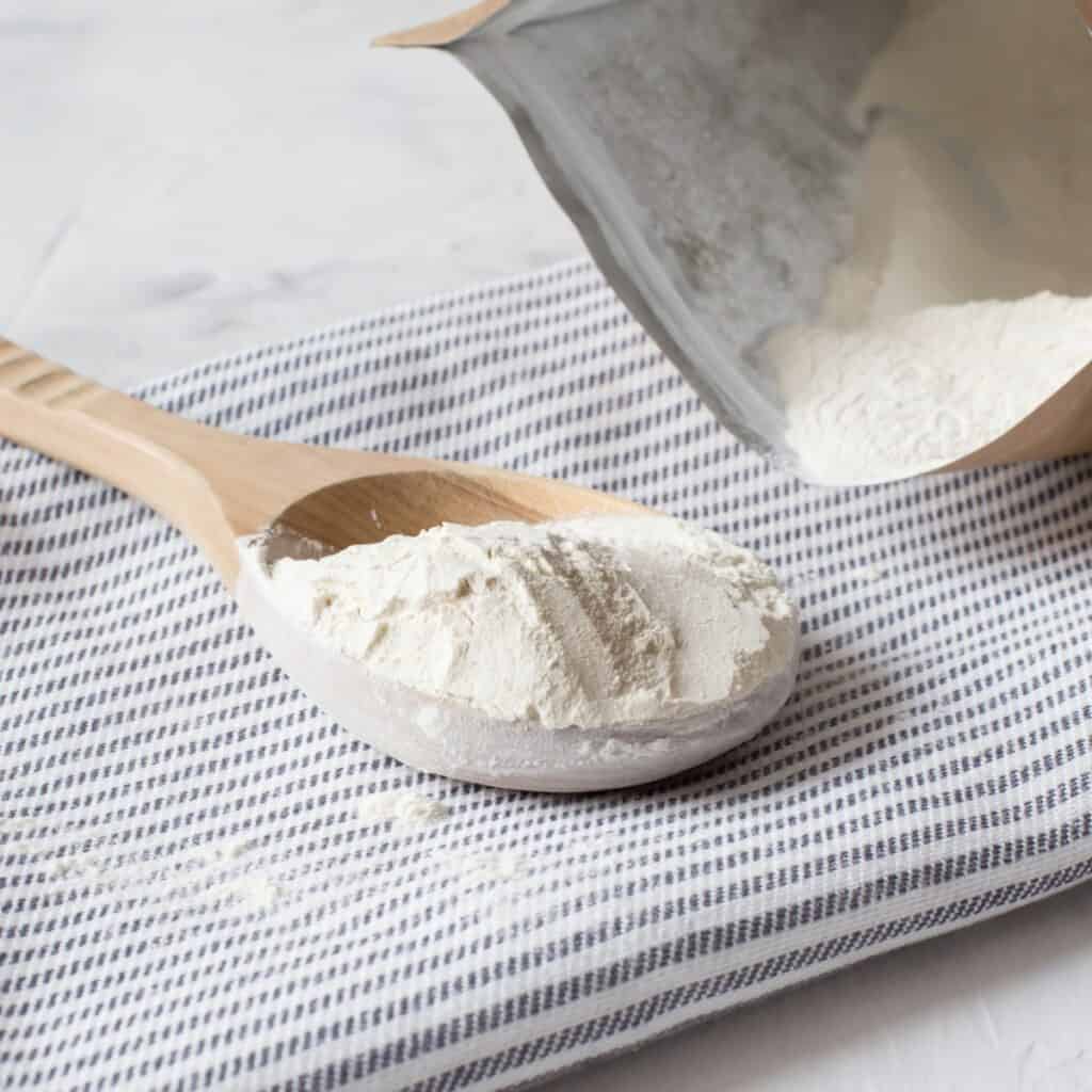 a spoon full of Xanthan Gum powder with the bag of Xanthan Gum next to it