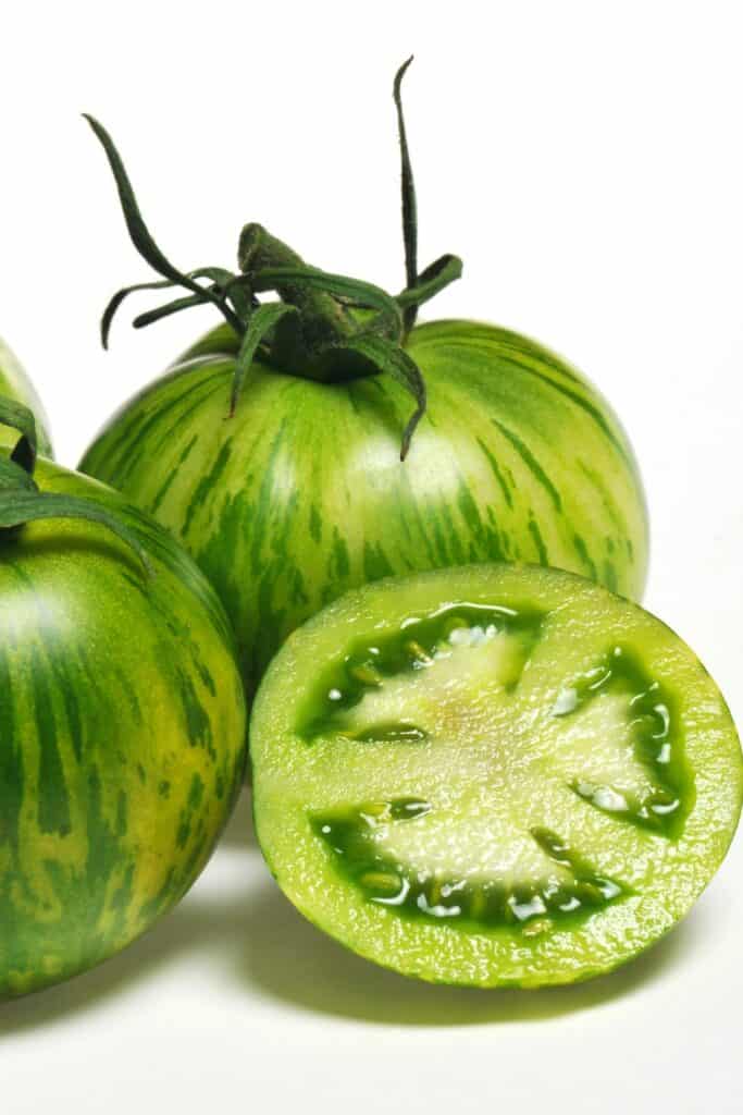 two whole zebra tomatoes with one cut in half on a white table