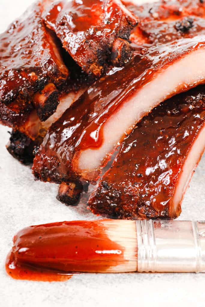 BBQ ribs covered in Carolina BBQ sauce with a brush next to them that's been dipped in the sauce