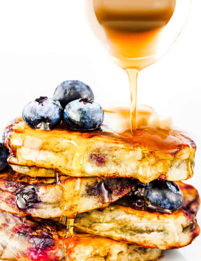 a stack of blueberry pancakes with syrup being poured on top