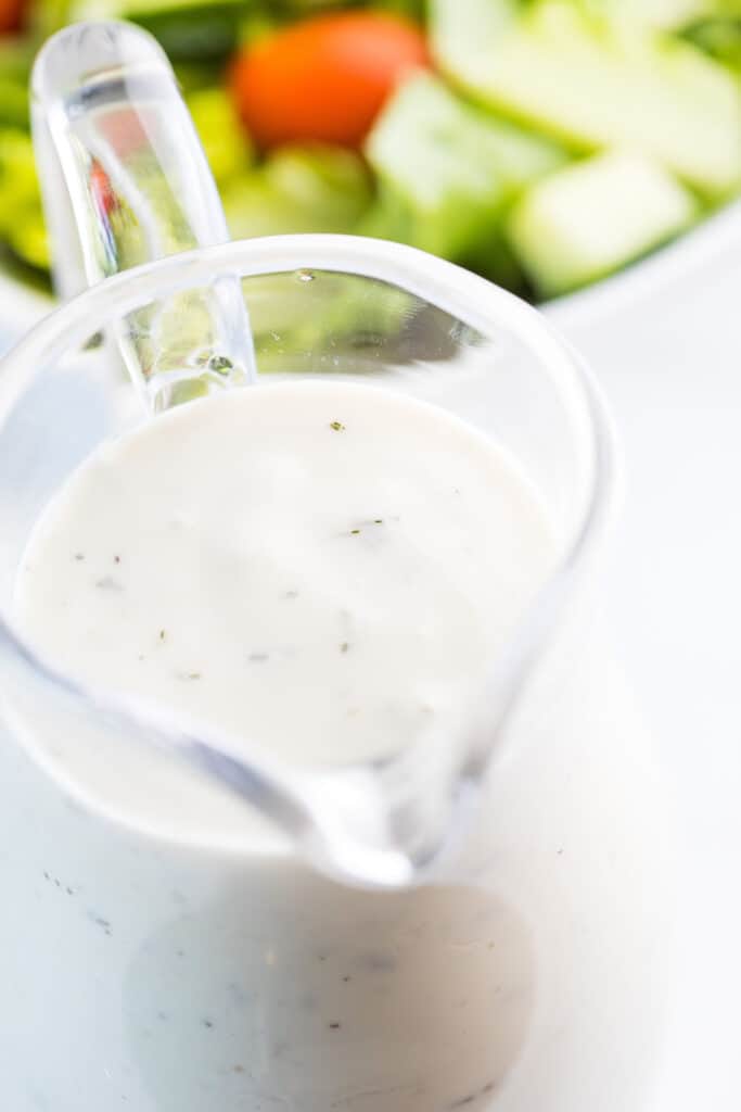 Garlic Dressing in a serving jug with a salad in the background.