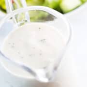 a close up image of Garlic Dressing in a serving jug with a salad in the background.