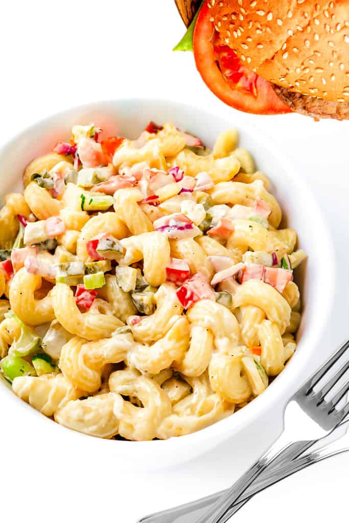 a bowl of Amish Macaroni Salad with forks and a hamburger in the background