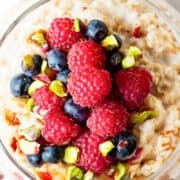 a close up image of a jar filled with overnight oatmeal and topped with mixed berries and chopped pistachios