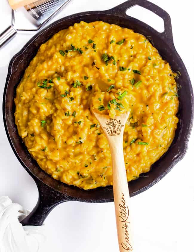 The cooked Saffron Risotto in a black pan with a wooden spoon and parmesan cheese in the background