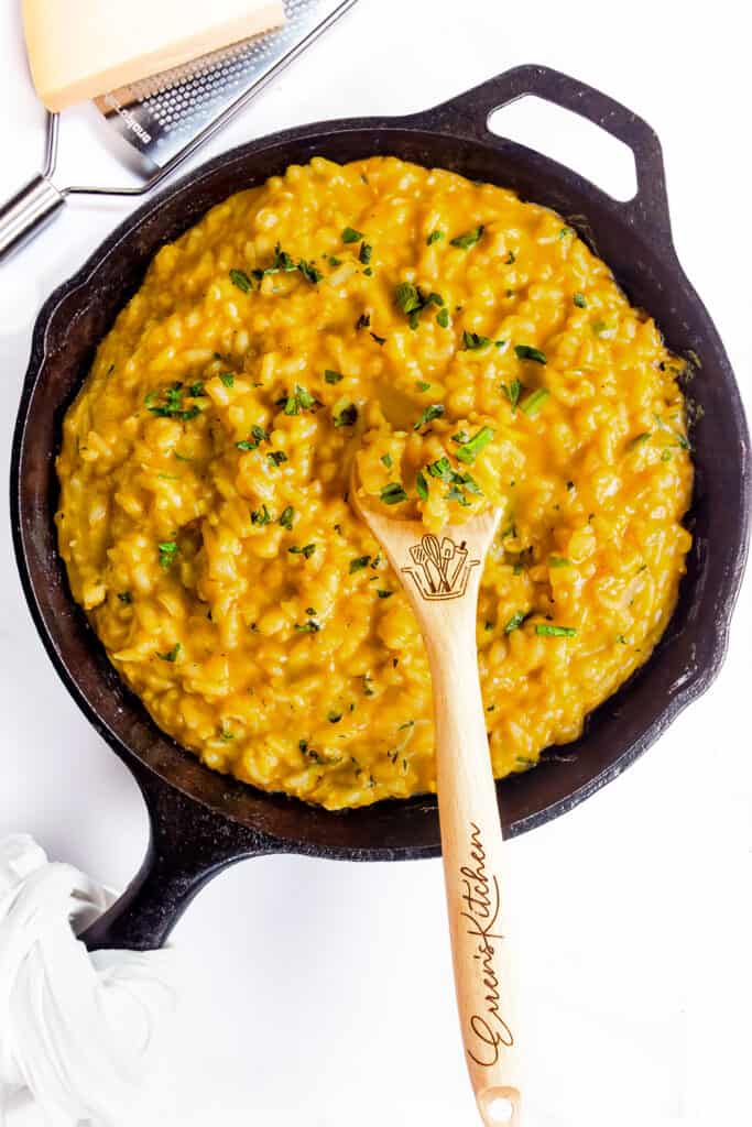 The cooked Saffron Risotto in a black pan with a wooden spoon and parmesan cheese in the background