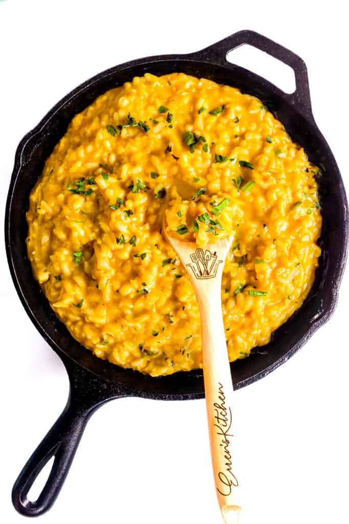 The cooked Saffron Risotto in a black pan with a wooden spoon