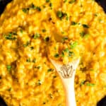 a close up image of The cooked Saffron Risotto in a black pan with a wooden spoon